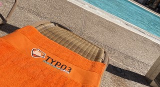 orangenfarbenes TYPO3 Surfcamp 2024 Handtuch am Pool